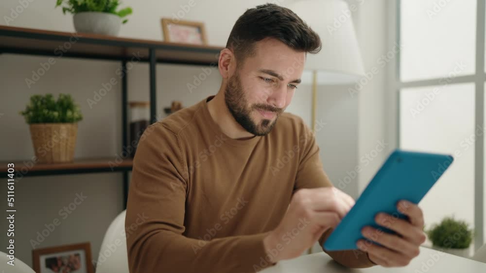 Young hispanic man using touchpad sitting on table at home Young hispanic man using touchpad sitting on table at home