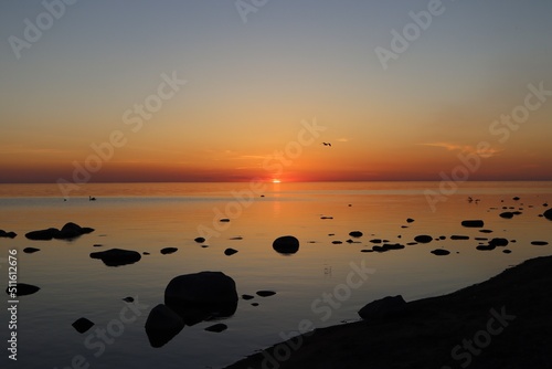 Sunset over calm Baltic sea  in Saulkrasti  Latvia. Sun shining from behind clouds  bright reflection on water  black shapes of boulders. Selective focus