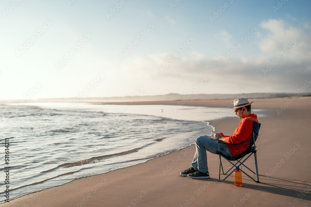 mature man sitting alone on beach outdoors looking at cell phone relaxed