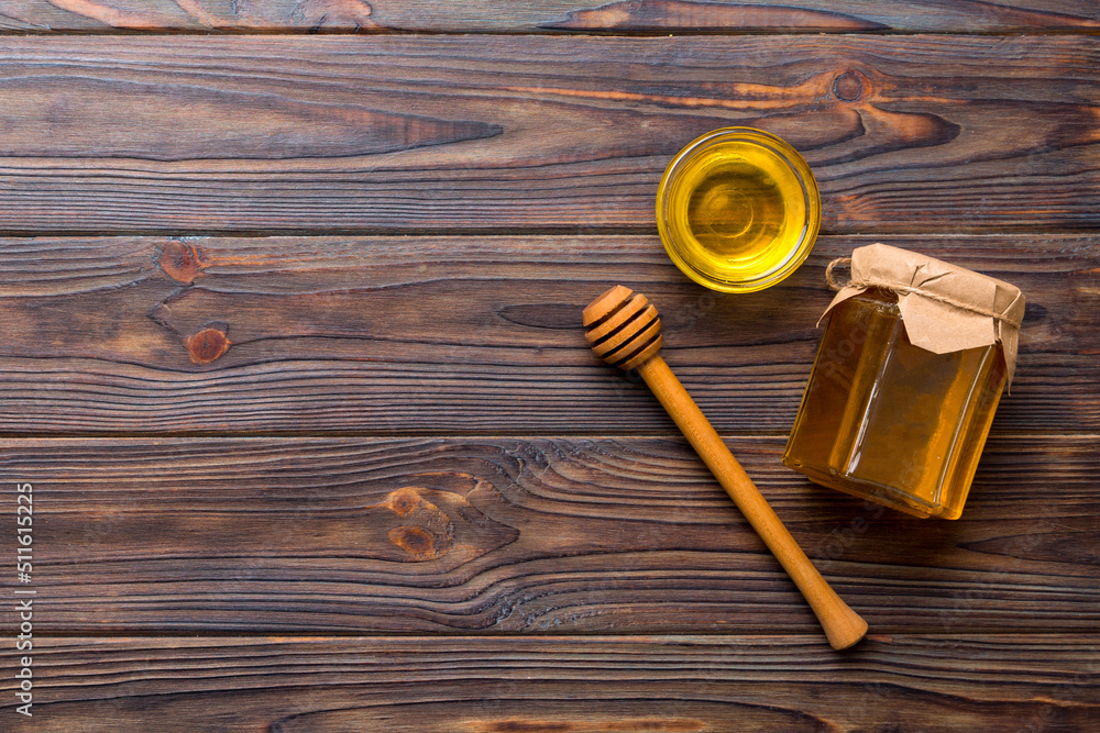 Glass jar of honey with wooden drizzler on colored background. Honey pot and dipper high above. Top view copy space