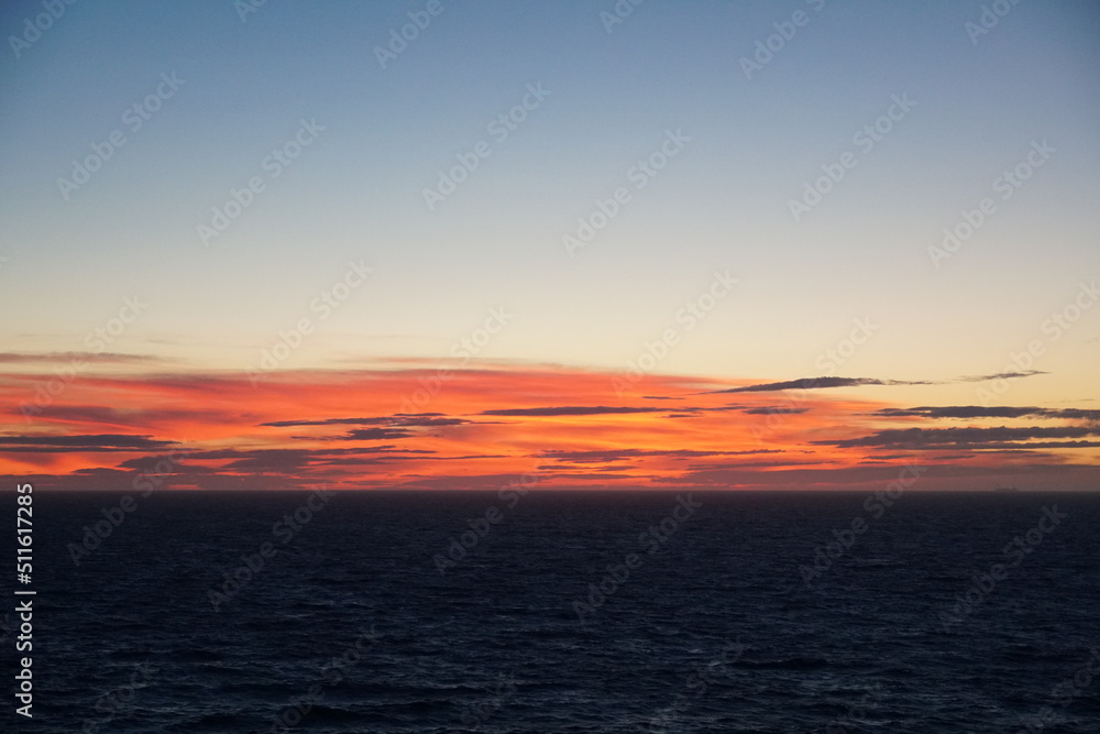 Sunset in Atlantic Ocean during calm weather in Summer season with the sun behind the horizon. Sunrays have orange colour. Picture was taken from the navigational bridge of the cargo container vessel.