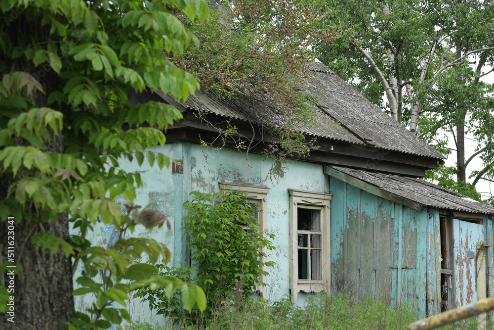 An old abandoned rural house with broken windows, overgrown with grass.