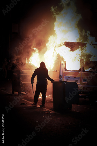 Man holding a baton in front of a burning police car