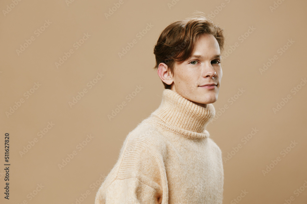 portrait of a pleasant, handsome man with long hair and freckles on his face in a textured beige sweater on a beige background. Empty space for layout portrait of a pleasant, handsome man with long hair and freckles on his face in a textured beige sweater on a beige background. Empty space for layout