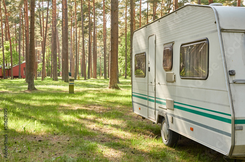 Caravan trailer parked on a green lawn in the evergreen pine forest. Travel destinations, leisure activity, eco tourism, camping site, transportation, RV. Freedom, wanderlust concept