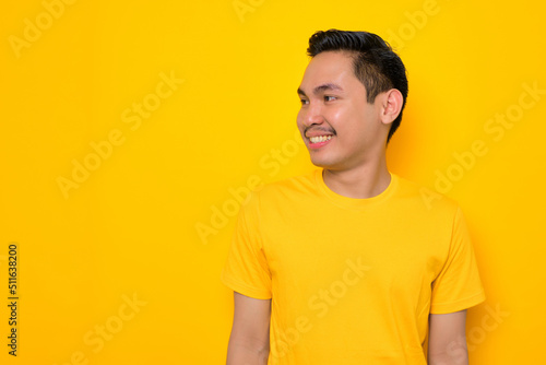 Cheerful young Asian man in casual t-shirt looking away at copy space isolated on yellow background. People lifestyle concept