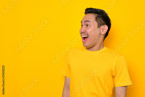 Excited young Asian man in casual t-shirt screaming at copy space with excitement isolated on yellow background. People lifestyle concept