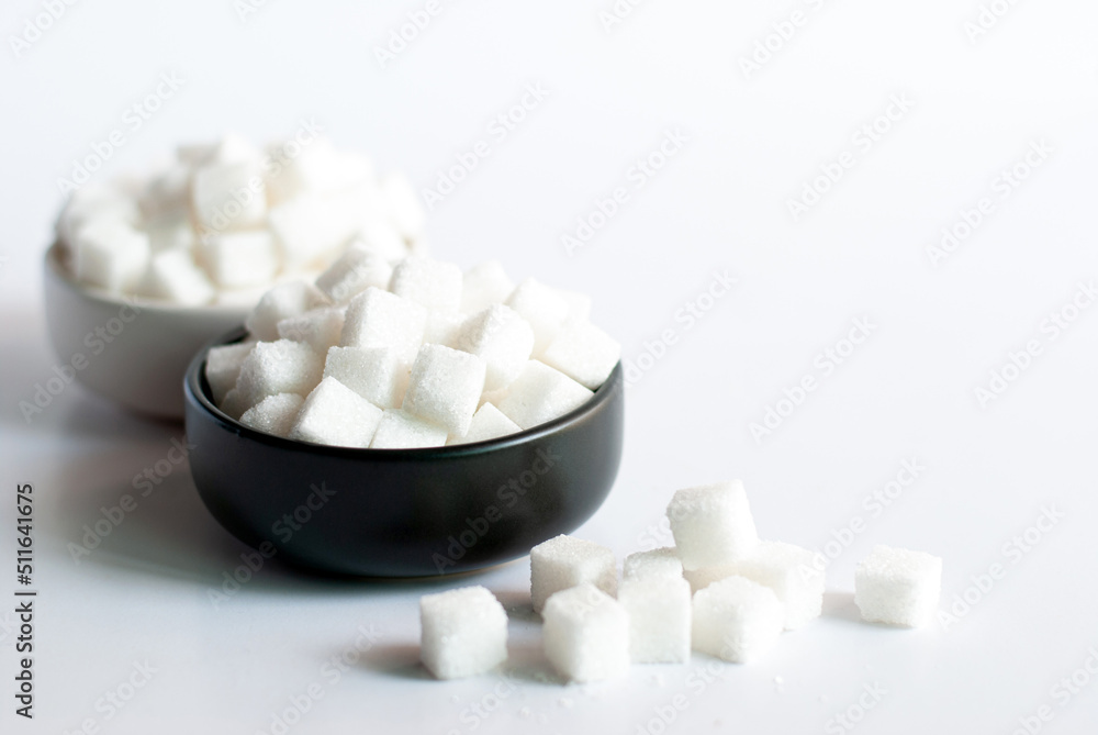 Sugar cubes in a black bowl and white bowl on white background. Sugar cubes in a black bowl and white bowl on white background.
