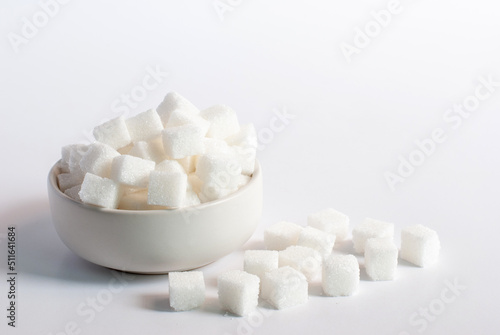 Sugar cubes in a white bowl on white background.