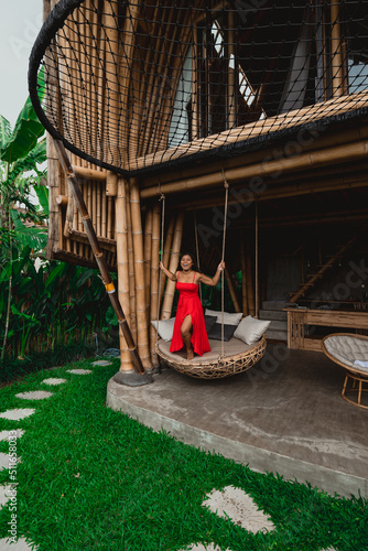 young female asian swinging in a red dress at a luxury bamboo villa