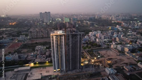 aerial orbiting dusk shot of under construction skyscraper with crane and workers with parallax effect with the smaller houses and buildings in the background shot at dusk in the city of gurgaon delhi photo