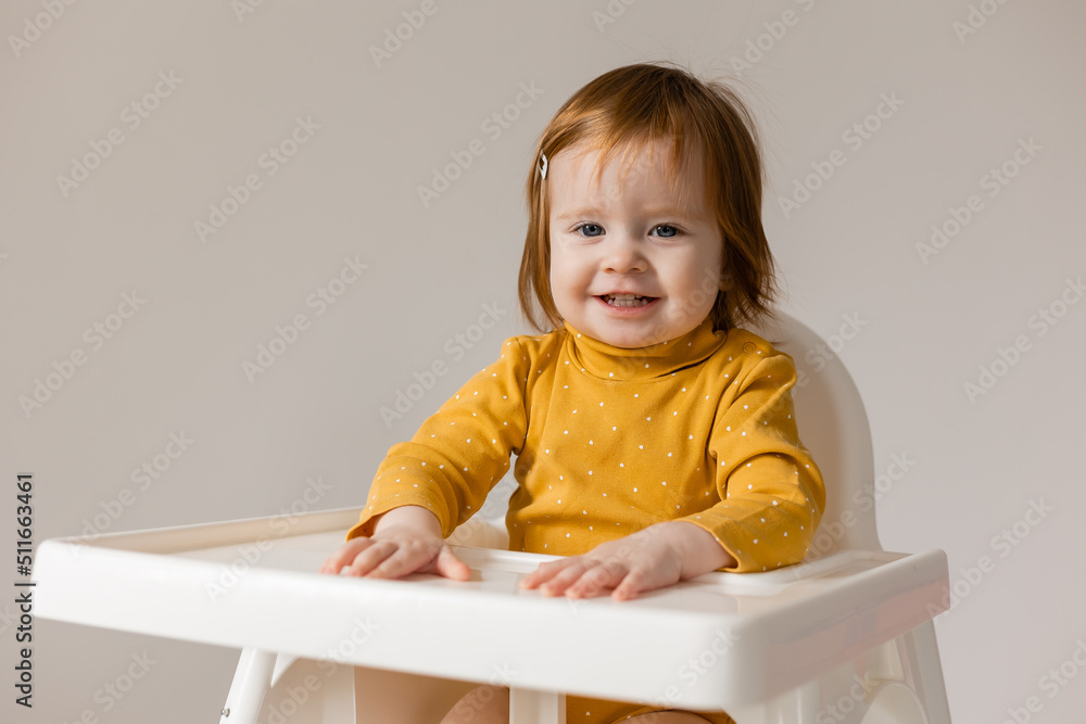 funny red-haired blue-eyed baby in a yellow bodysuit sitting in a white high chair funny red-haired blue-eyed baby in a yellow bodysuit sitting in a white high chair