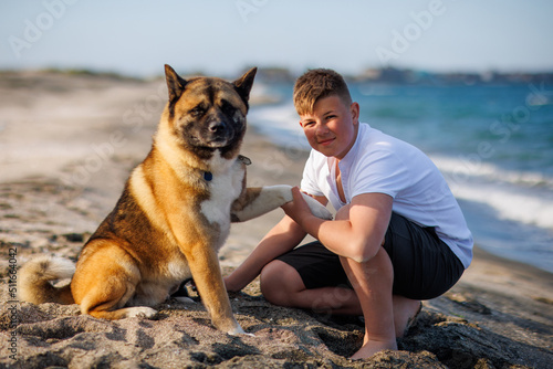 Teenage guy with blond hair and leash in hands plays and walks with dog of Akina Inu breed on wild beach along Black Sea photo