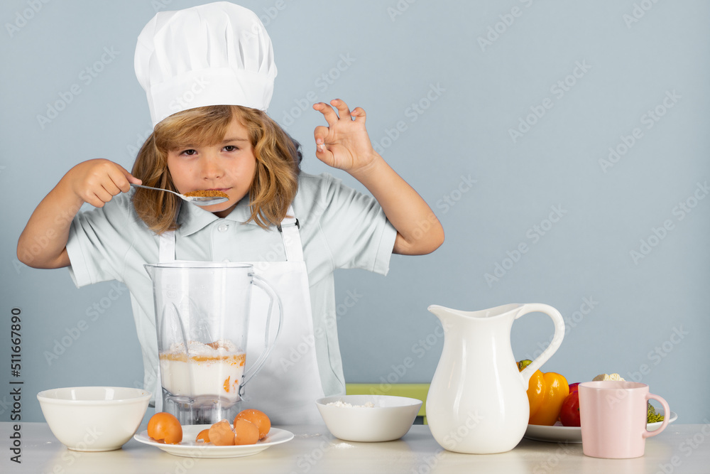 Child chef cook prepares food on isolated grey studio background. Kids cooking. Teen boy with apron and chef hat preparing a healthy vegetables meal in the kitchen. Child chef cook prepares food on isolated grey studio background. Kids cooking. Teen boy with apron and chef hat preparing a healthy vegetables meal in the kitchen.