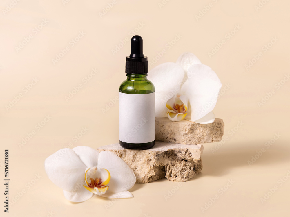 Green dropper glass bottle near white orchid flowers on light yellow, Mockup. Skincare product