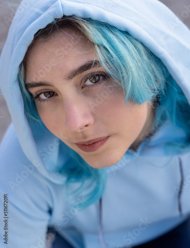 Blue haired Teenage girl in light blue oversize hoodie lookinginto a camera from down