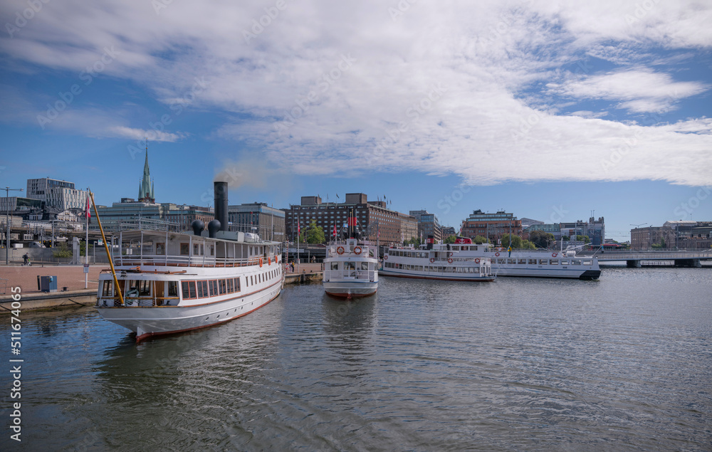 Commuter boats and old steam boats at the Town City Hall pier smoke from chimney when heating up of boiler a sunny summer day in Stockholm
