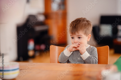 Little toddler boy sitting at wooden table sadly looking sideways
