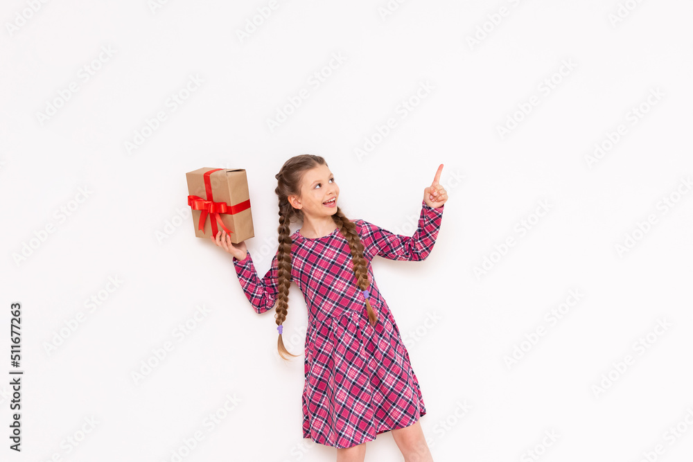 A little girl holds a gift and points up at your advertisement on a white isolated background. The concept of the holiday. A little girl holds a gift and points up at your advertisement on a white isolated background. The concept of the holiday.
