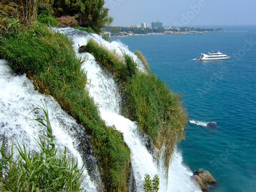Waterfall with water falling from a great height into the sea. In the background is a ship photo