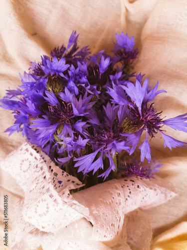 bouquet of purple cornflowers with white vintage ribbon on the table at sunset