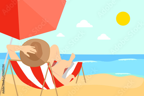 Woman in bikini and hat lying on a sun lounger sunbathing in front of the sea and protected by an umbrella
