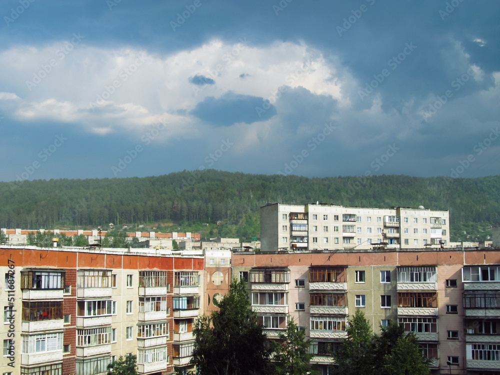 Residential high-rise buildings in Russia against the backdrop of a wooded hill and cloudy sky