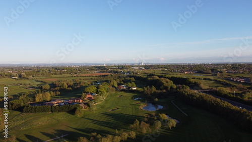 Aerial view looking down onto a golf course surrounded by green fields with the Manchester skyline in the distance. © ReayWorld