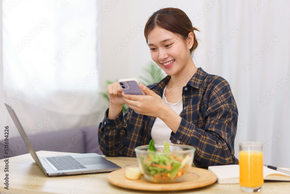 Lifestyle in living room concept, Young Asian woman using smartphone and eating vegetable salad Lifestyle in living room concept, Young Asian woman using smartphone and eating vegetable salad