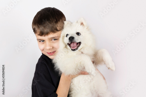 A young boy smiles and holds a young dog in his friend's arms, they play together, the dog tries to lick his friend, to thank him. The boy and his dog are playing at home © Мар'ян Філь