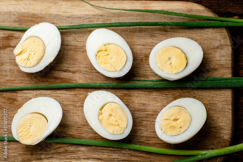 Halves of boiled chicken eggs with green onion pods on a wooden background.