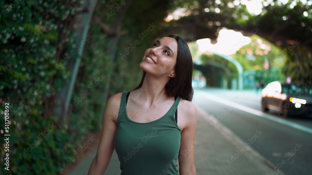 Joyful girl in green top walks through an arch covered with green plants along the road. Young woman smiling walks along the sidewalk looking at wall overgrown with green leaves Joyful girl in green top walks through an arch covered with green plants along the road. Young woman smiling walks along the sidewalk looking at wall overgrown with green leaves