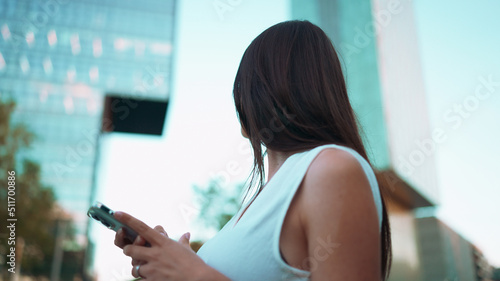 Beautiful woman with freckles and dark loose hair wearing white top is looking at map on mobile phone. Pretty girl uses smartphone to locate