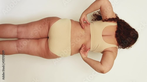 Vertical rearview shot of long-haired overweight, adipose and fat woman holding excess folds on her body under shoulder blades. Edema fibrosis skin. Cellulite back and legs. Need liposuction surgery photo