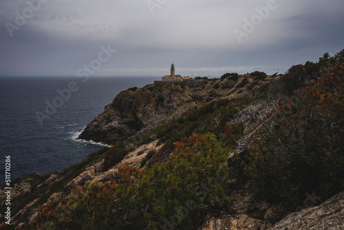 Biała latarnia morska na skalistym klifie w pochmurny dzień. Latarnia położona jest na wschodnim wybrzeżu Majorki. 