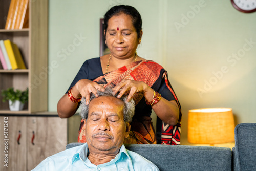 wife massaging head of relaxed husband at home while sitting on sofa - concept of family, senior couple and bonding.