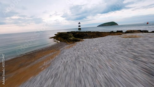 FPV Aerial view of penmon point light house, fast low flying towards the light house then around showing the landscape area. birds eye view North Wales UK photo