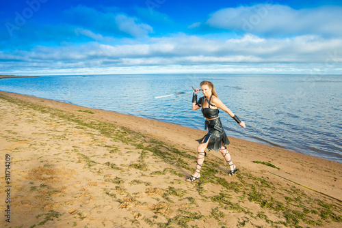 angry Viking girl wearing leather armor with falchion in her hand is running at the waterside photo