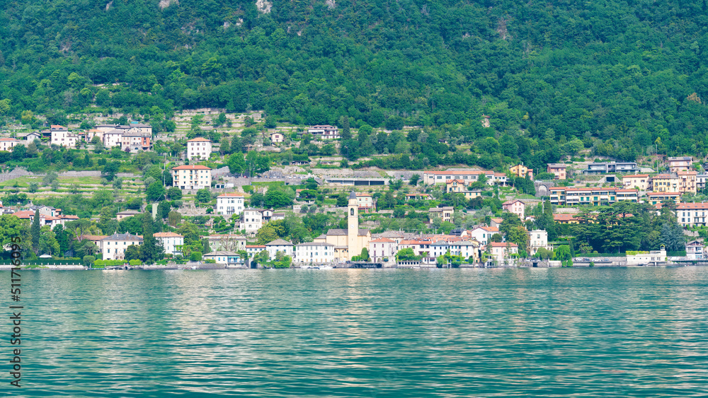 Typical italian village on the coastline of Lake Como, Lombardy, Italy. Turquoise waters in the foreground. Green trees in the background.