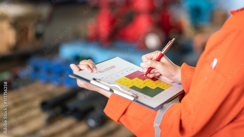 The manager is using ballpoint pen to marking on the risk assessment matrix at "High risk" level, with blurred background of factory place. Industrial and business working photo. - obrazy, fototapety, plakaty 