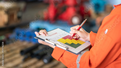 The manager is using ballpoint pen to marking on the risk assessment matrix at "High risk" level, with blurred background of factory place. Industrial and business working photo.
