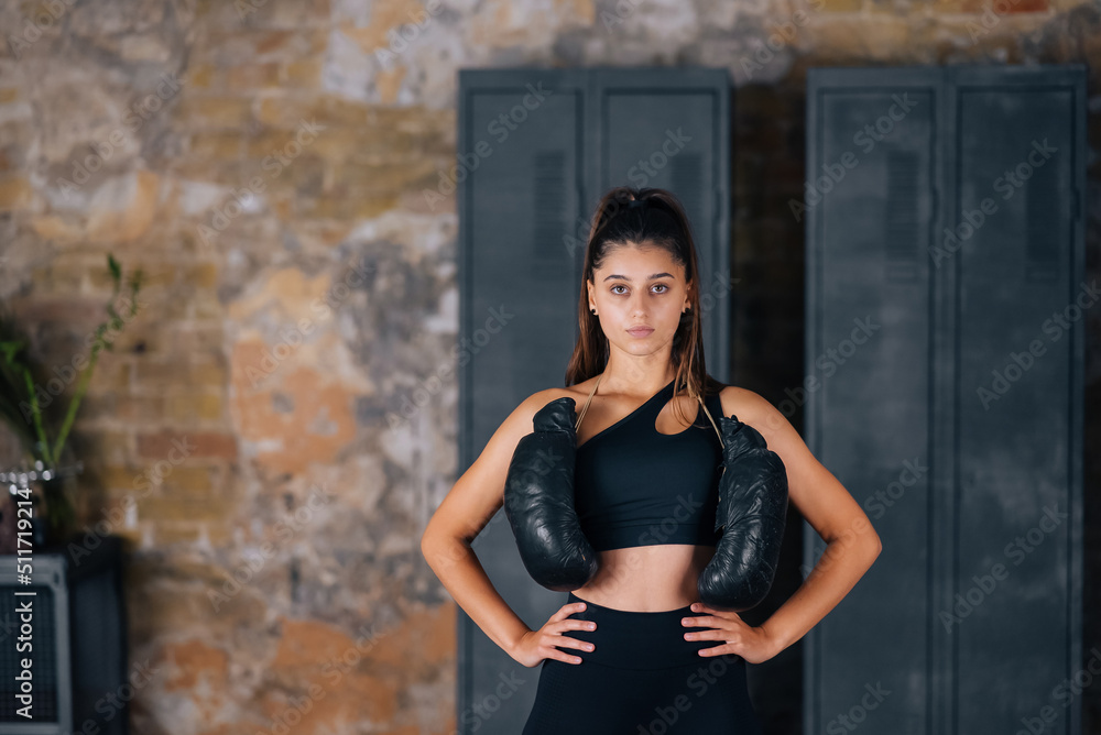 Fototapeta premium Sporty woman in sportswear posing on camera with boxing gloves.