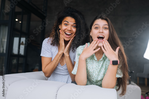 Two girls sit on the back of the sofa  look at the cameras and smile