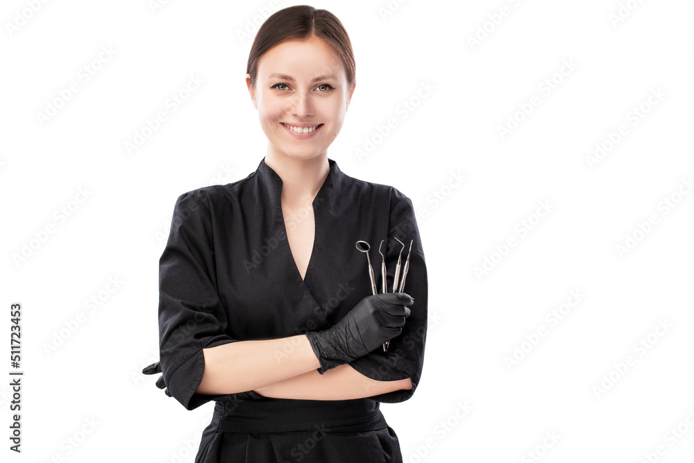 Portrait of happy young smiling girl dental doctor. Dressed in a black robe. Evenly standing with crossed hands holding medical instruments on a white background Portrait of happy young smiling girl dental doctor. Dressed in a black robe. Evenly standing with crossed hands holding medical instruments on a white background