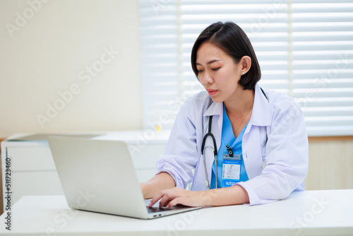 Working on laptop. Female asian doctor sitting on desk office at modern medical center. Healthcare medical and medicine concept.