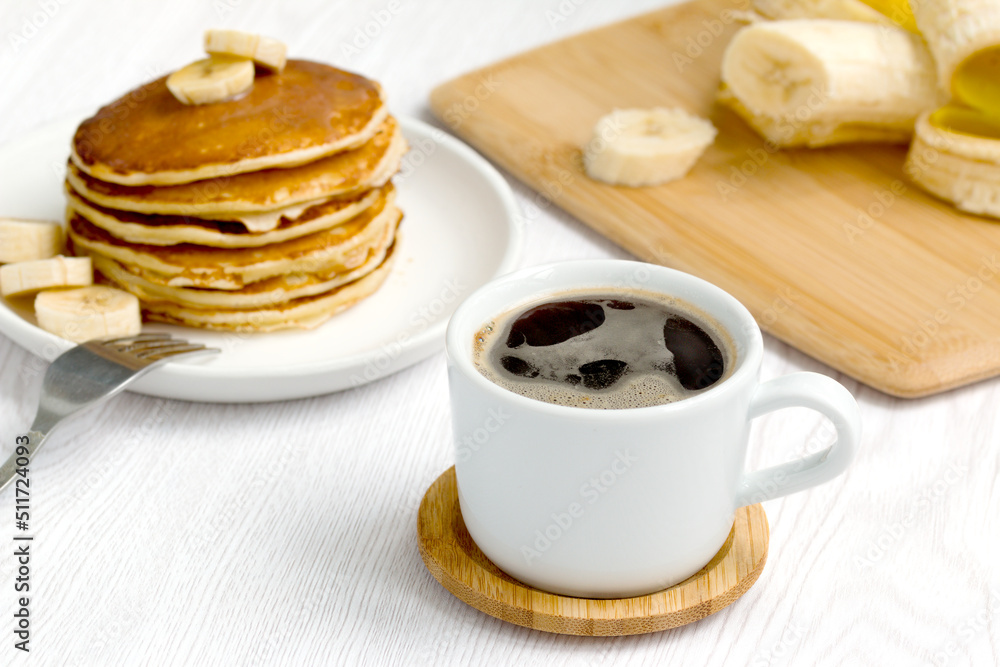 a cup of black coffee on the background of a stack of pancakes with bananas a cup of black coffee on the background of a stack of pancakes with bananas