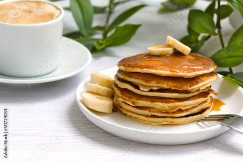 a stack of delicious pancakes with syrup, bananas and a cup of aromatic coffee