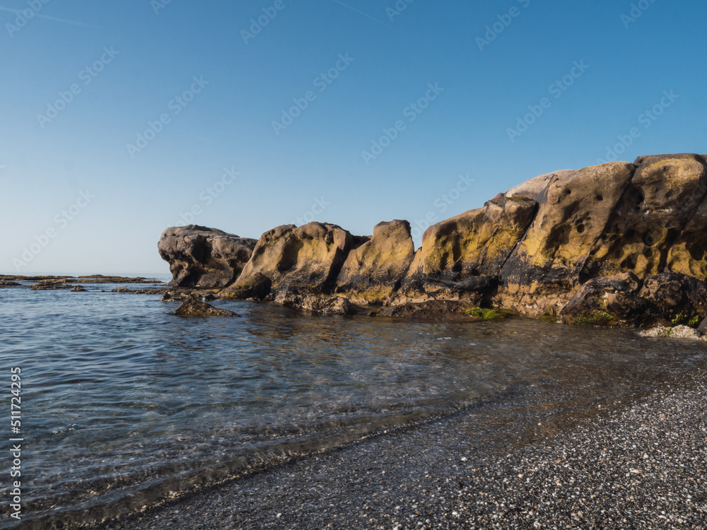 Small stone beach shore in the mediterranean sea on the Costa del Sol. Transparent water and eroded rocks in Manilva