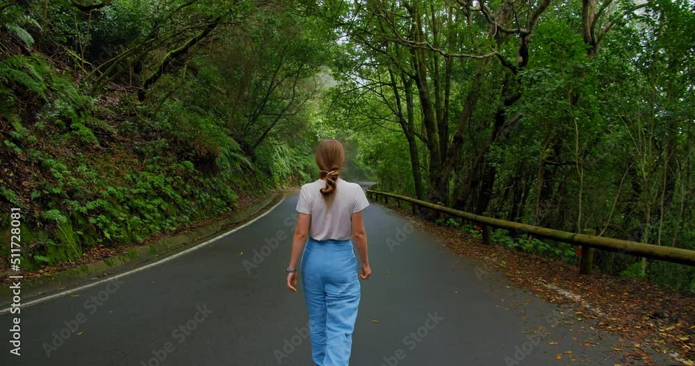 Rear view of a young woman walking on paved road in the Rainforest Anaga rural park , Tenerife north, Canary islands, Spain Rear view of a young woman walking on paved road in the Rainforest Anaga rural park , Tenerife north, Canary islands, Spain