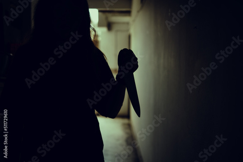 The shadow of a female murderer stood terrifyingly holding a knife and lit from behind.Scary horror or thriller movie mood or nightmare at night Murder or homicide concept.